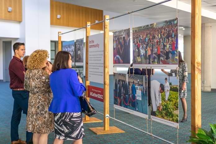 A few people examine a wall of hanging photos of Convention Center community activities
